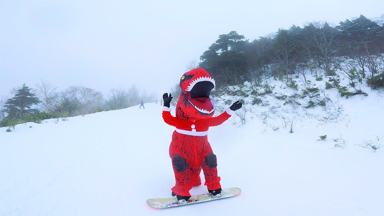 A red skinned dino, in a santa suit, on a snowboard, looking the the camera, while enjoying the slopes.