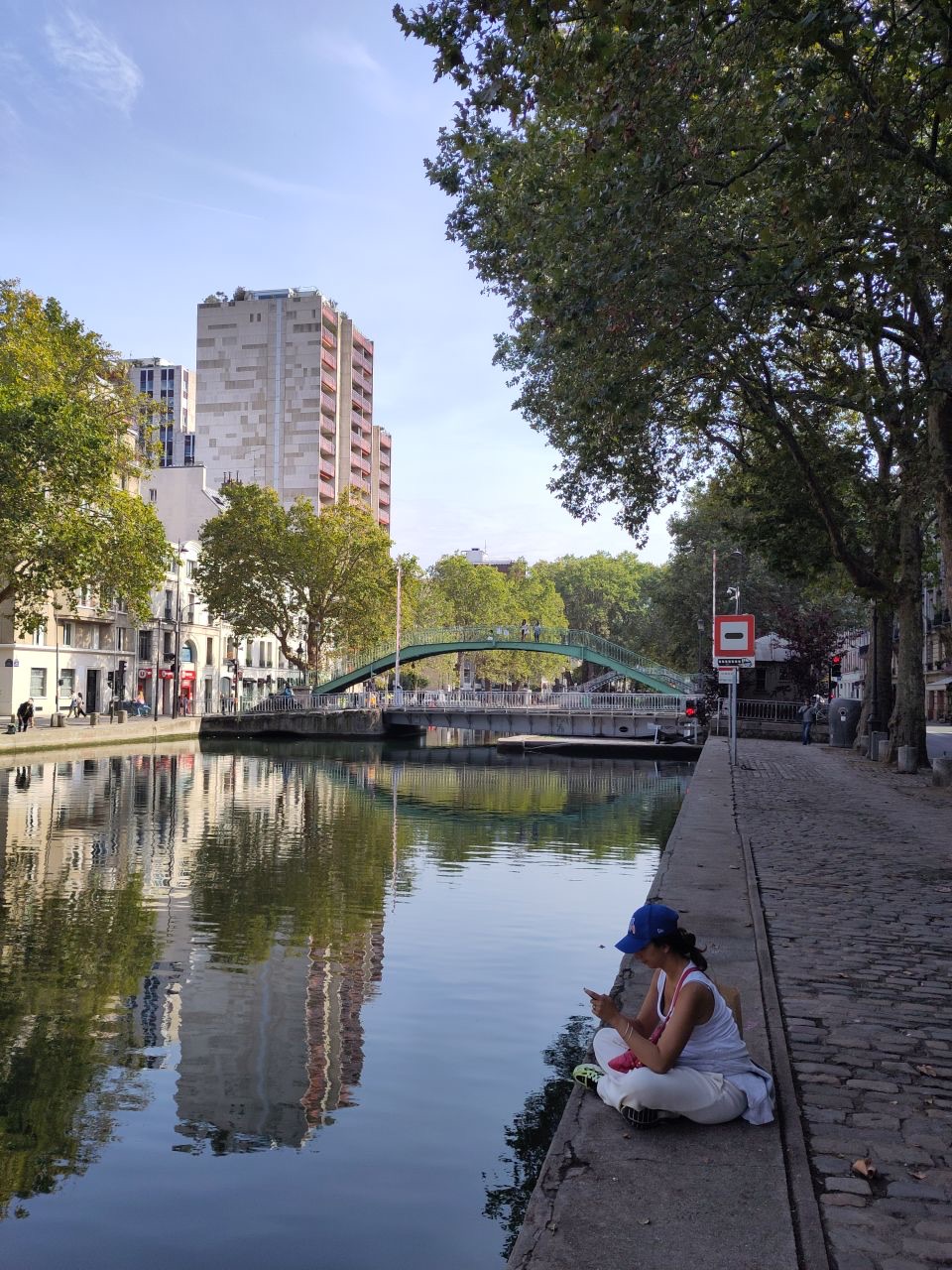 Canal with paved quai on right, modern buildings on left, and bridges in background.
